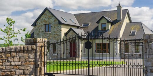 Grande maison en pierre, entourée d'un portail design noir, conçue par SJH Menuiserie.