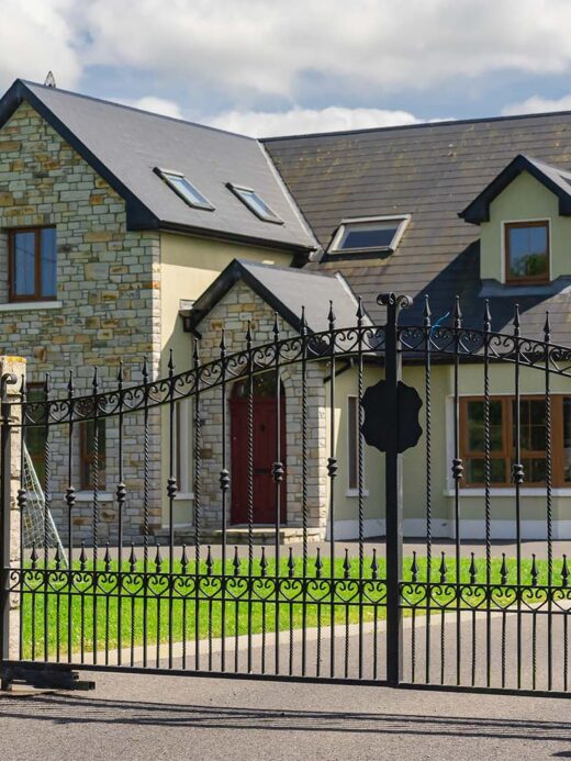 Grande maison en pierre, entourée d'un portail design noir, conçue par SJH Menuiserie.