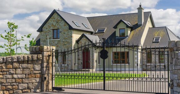Grande maison en pierre, entourée d'un portail design noir, conçue par SJH Menuiserie.