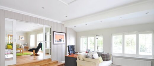 Séjour : parquet, canapé blanc, volets modernes. Une pièce attenante visible offre un confort supplémentaire.