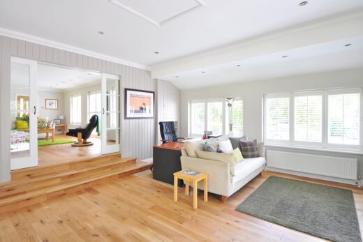 Séjour : parquet, canapé blanc, volets modernes. Une pièce attenante visible offre un confort supplémentaire.